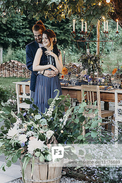 Glückliche Braut und Bräutigam umarmen sich an festlich gedeckter Tafel im Freien