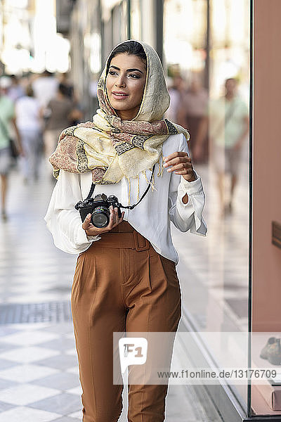 Spanien  Granada  junge arabische Touristin mit Hidschab  die beim Einkaufen in der Stadt eine Fotokamera benutzt
