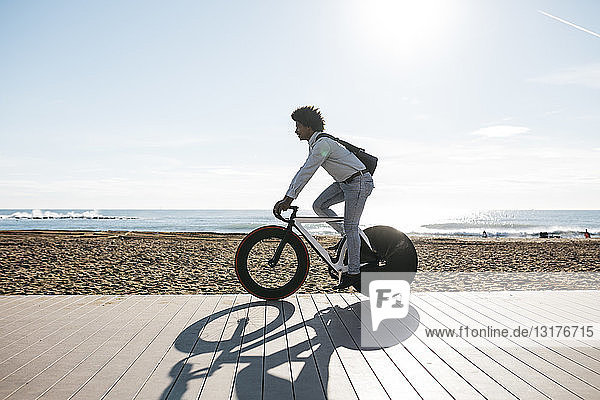 Mid adult man riding bicykle on a beach promenade  listening music