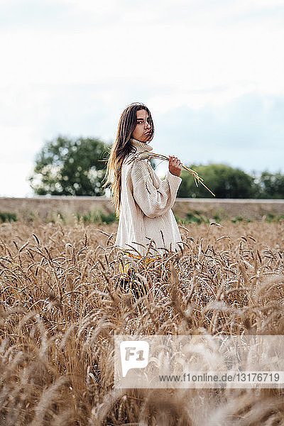 Junge Frau in übergroßem Rollkragenpullover im Maisfeld stehend