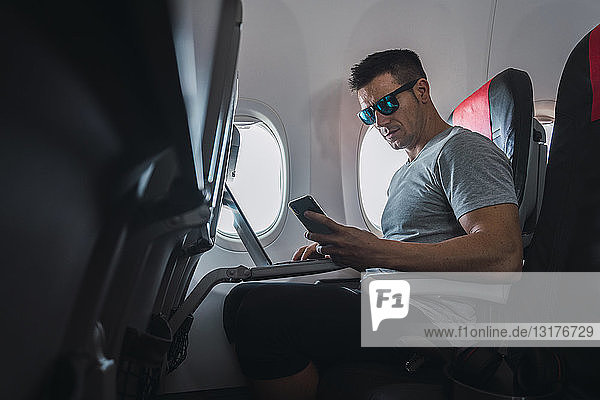 Mann im Flugzeug  mit Smartphone und Laptop