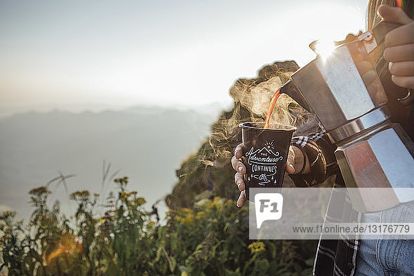 Nahaufnahme einer Frau auf einer Wanderung bei Sonnenaufgang  die Kaffee in eine Tasse gießt