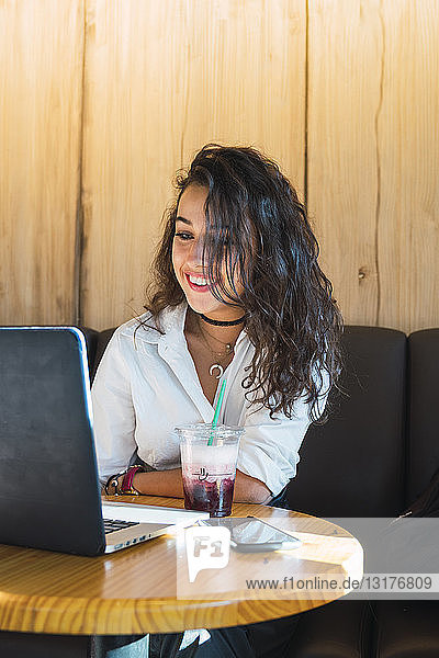 Portrait of smiling young woman in a coffee shop using laptop