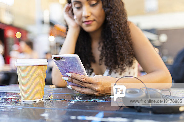 Junge Frau sitzt an einem Tisch und schaut auf ihr Handy