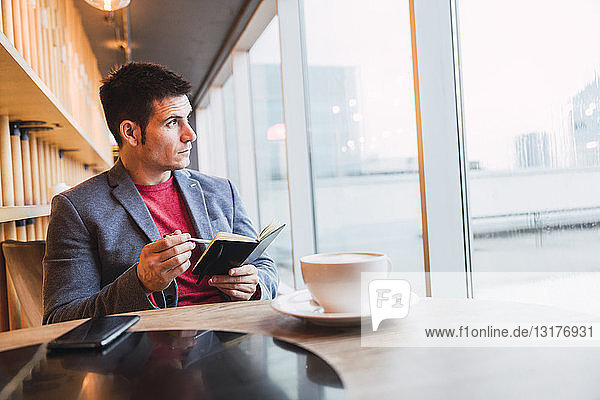 Businessman sitting in restaurant drinking coffee and checking his notebook