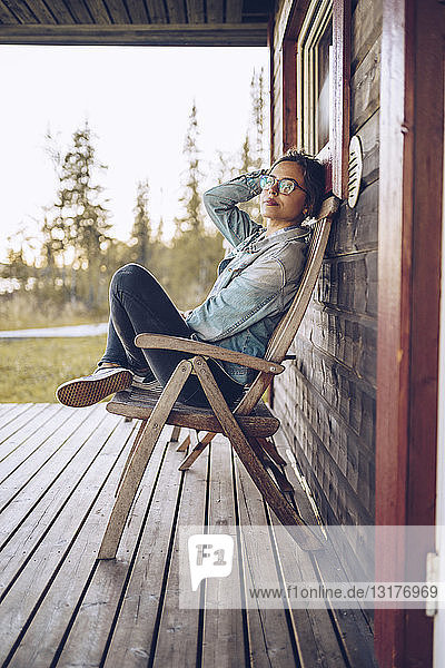Schweden  Lappland  Porträt einer jungen Frau  die auf einem Stuhl auf einer Veranda sitzt und sich entspannt