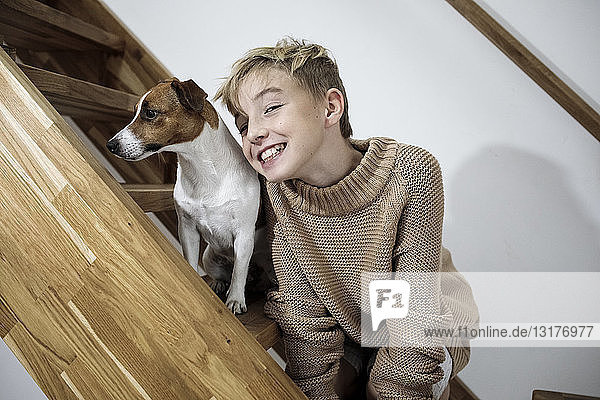 Porträt eines grinsenden Jungen und seines Jack Russel Terriers auf der Treppe zu Hause