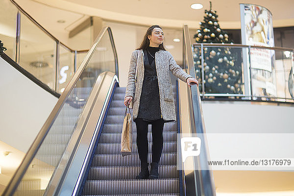 Junge Frau mit Einkaufstasche auf der Rolltreppe in einem Einkaufszentrum zur Weihnachtszeit