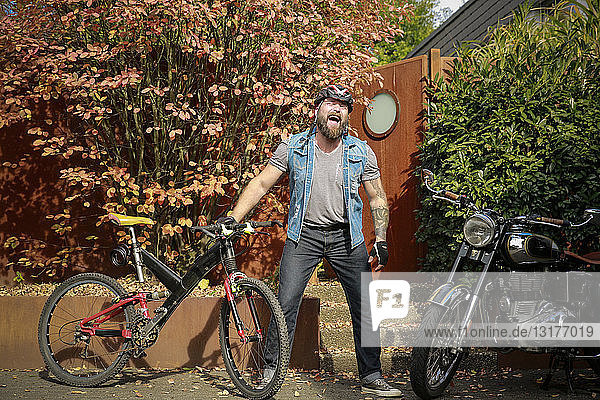 Lachender Mann steht zwischen Motorrad und Fahrrad