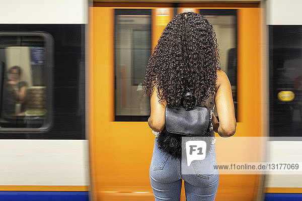 UK  London  Rückansicht einer jungen Frau  die am U-Bahn-Bahnsteig wartet