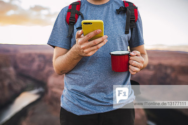 Junger Mann hält roten Becher und benutzt Smartphone