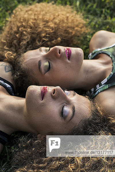 Porträt von geschminkten Zwillingsschwestern  die nebeneinander auf einer Wiese liegen
