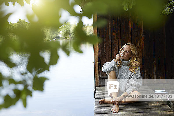 Lächelnde  entspannte Frau sitzt auf einem Holzsteg an einem abgelegenen See