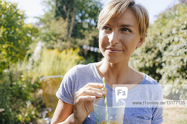 Porträt einer Frau  die im Garten ein Erfrischungsgetränk trinkt