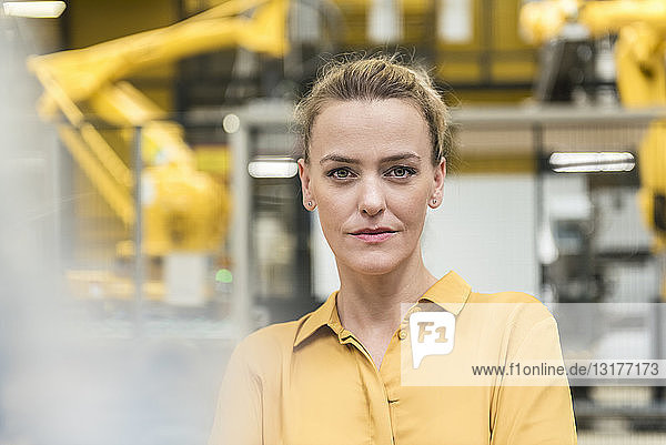Porträt einer selbstbewussten Frau in einer Fabrikhalle mit Industrieroboter