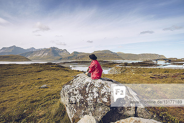 Norway Lofoten man wearing red rainjacket sitting on a rock looking at view