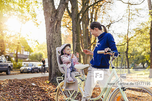 Mutter und Tochter fahren Fahrrad  das Baby trägt einen Helm und sitzt im Kindersitz