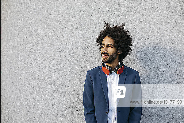 Smiling young businessman with headphones at a wall