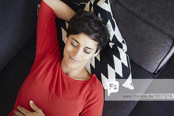 Lächelnde Frau liegt zu Hause mit geschlossenen Augen auf der Couch