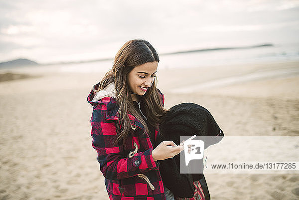 Lächelnde junge Frau mit Smartphone am Strand