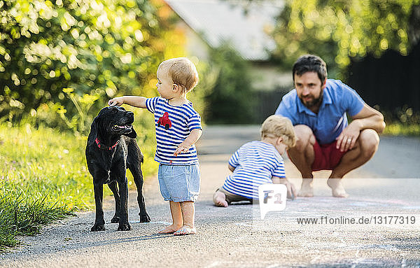 Kleines Mädchen streichelt Hund  während der Vater sie aus dem Hintergrund beobachtet