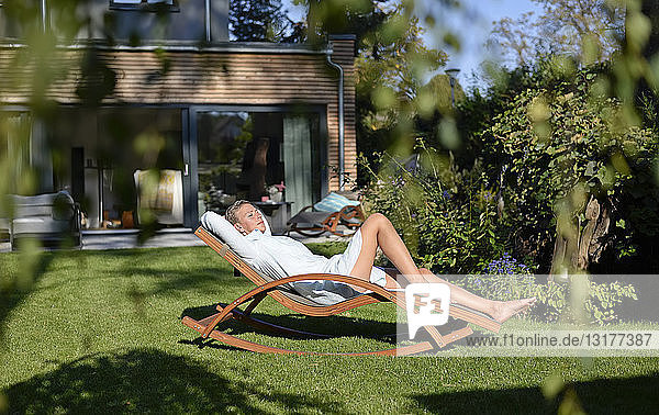 Frau entspannt sich auf Liegestuhl in ihrem Garten