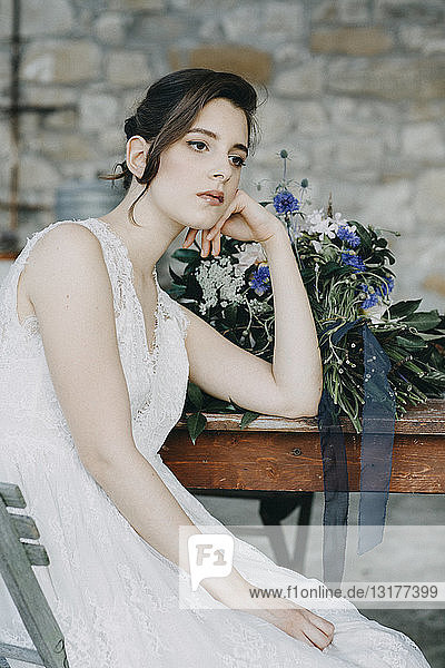 Nachdenkliche junge Frau im Brautkleid am Tisch sitzend