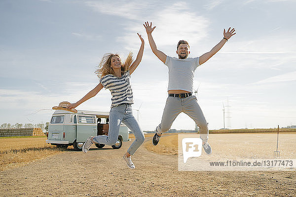 Überschwängliches Paar springt auf Feldweg am Wohnmobil in ländlicher Landschaft