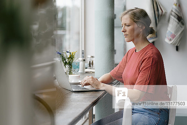 Junge Frau mit Laptop am Fenster in einem Cafe