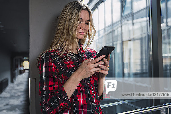 Junge Frau in modernem Bürogebäude schaut auf Handy