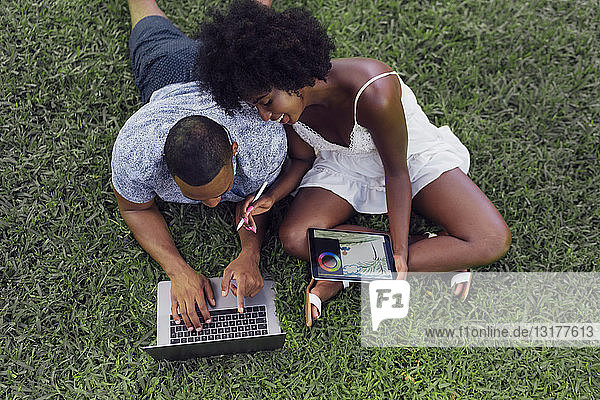 Junges Paar mit Tablett und Laptop auf einem Rasen in einem Park