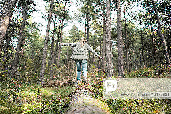 Kleines Mädchen balanciert auf einem Baumstamm im Wald