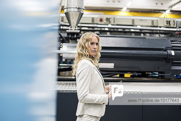 Frau mit Tablette an der Maschine in der Fabrikhalle  die sich umsieht