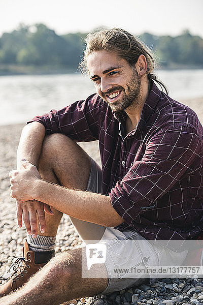 Lächelnder junger Mann sitzt am Flussufer