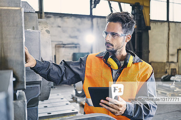Man with tablet wearing protective workwear working in factory