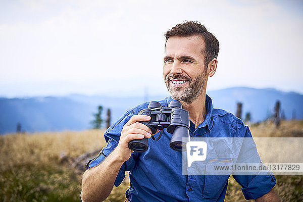 Lächelnder Mann mit Fernglas beim Wandern in den Bergen