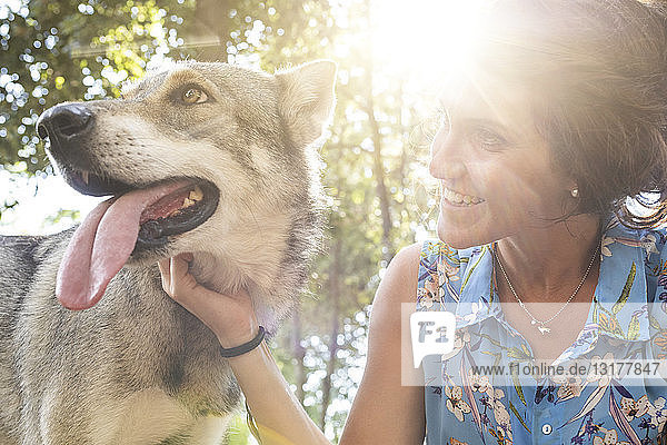 Lächelnde junge Frau streichelt ihren Hund im Gegenlicht