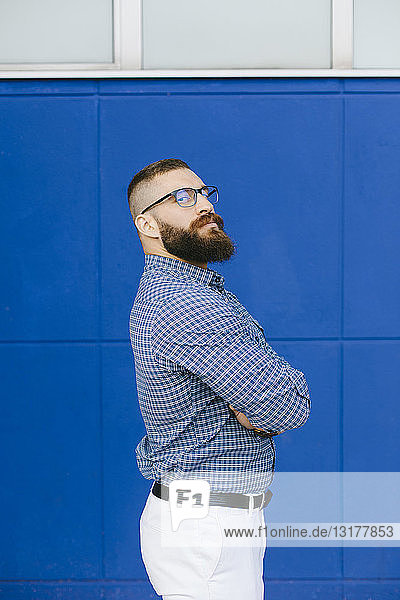 Portrait of bearded hipster businessman wearing plaid shirt standing in front of blue background