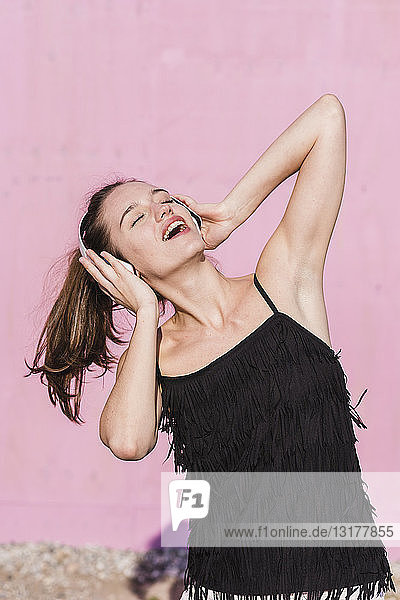 Glückliche junge Frau mit Kopfhörern vor rosa Wand