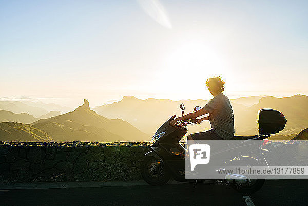 Spain  Canary Islands  Gran Canaria  man on motor scooter watching sunset over mountainscape