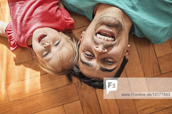Porträt eines Vaters und einer kleinen Tochter  die zu Hause auf dem Boden liegen und sich amüsieren