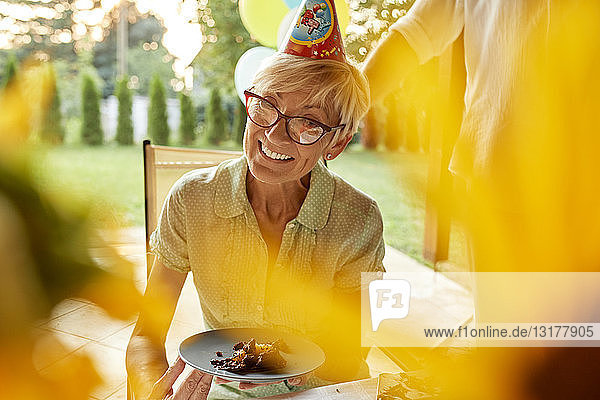 Lächelnde reife Frau hält Teller mit Kuchen auf einer Geburtstagsgartenparty