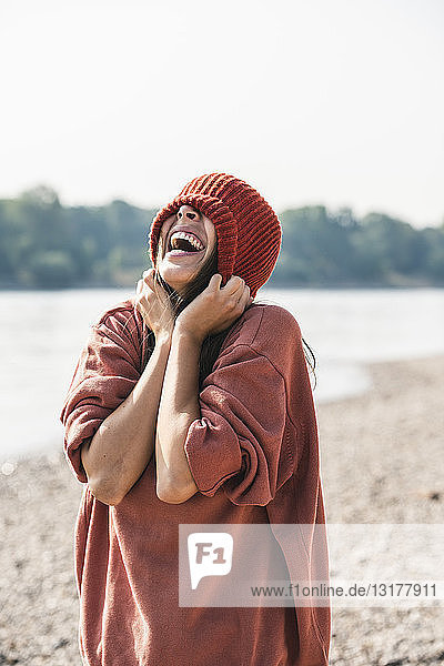 Unbeschwerte junge Frau mit Wollmütze am Flussufer