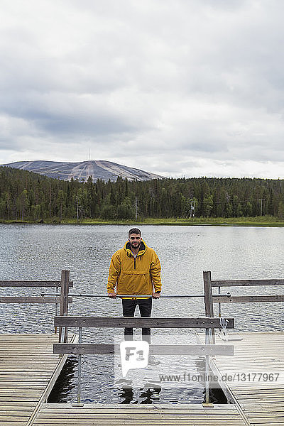 Finnland  Lappland  Mann balanciert auf einer Rute auf einem Steg über einem See