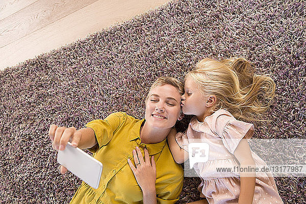 Lächelnde Mutter und Tochter auf dem Teppich liegend  die ein Selfie