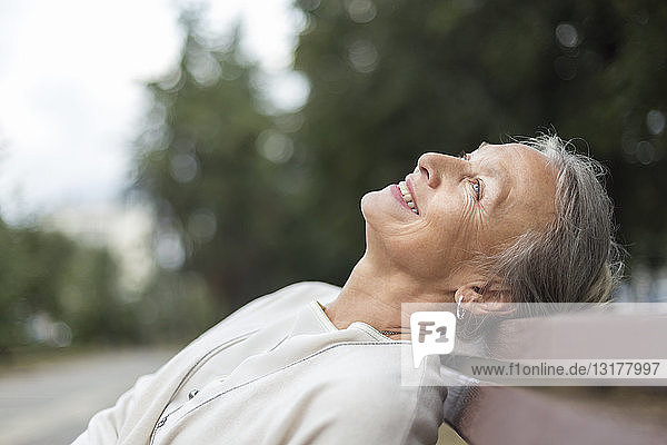 Lächelnde ältere Frau entspannt auf einer Bank und schaut auf