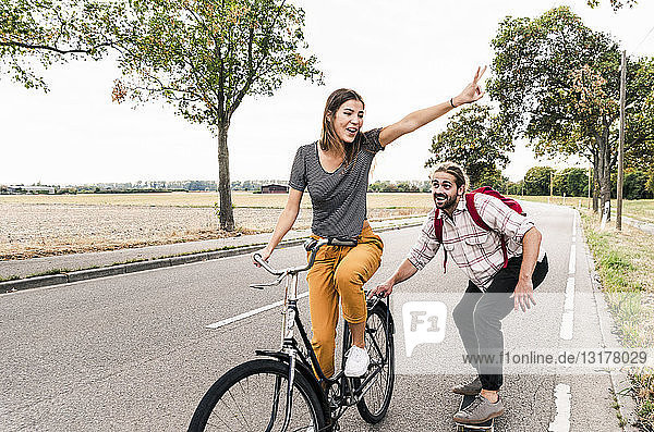 Happy young couple with bicycle and skateboard on country road