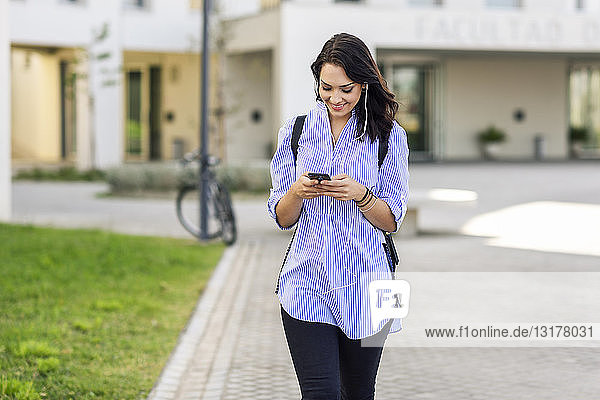 Portrait of smiling student using smartphone and earphones