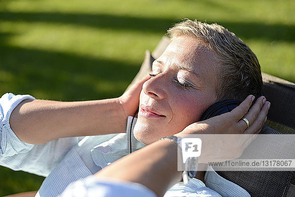 Porträt einer Frau  die im Garten mit Kopfhörern Musik hört