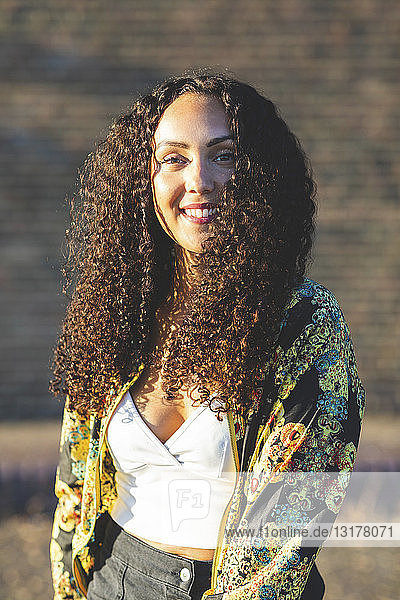 Porträt einer lächelnden jungen Frau mit lockigem Haar im Freien